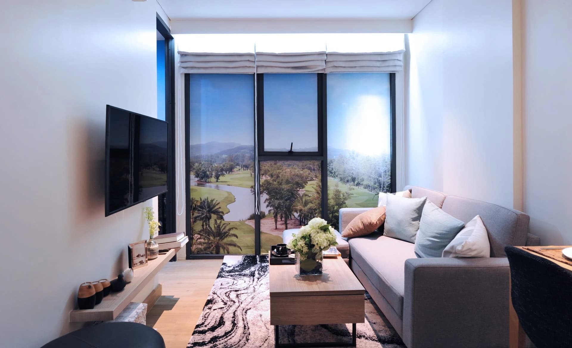 Show unit, type 1B: living room with a grey sofa and glass doors onto a green, open outlook